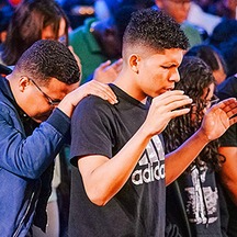 Group of young men bowed in prayer, hands on each other's shoulders