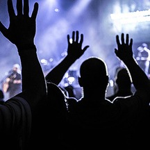 Congregation with hands raised in worship under stage lighting