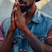 Man in a denim jacket with hands clasped in prayer